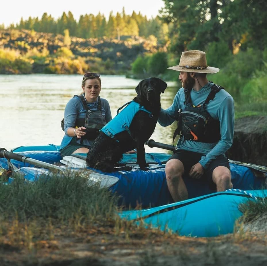 Eddy the rafting dog sits with her humans on the river bank.
